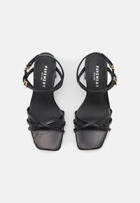 Sandales en cuir noir à bouts carrés, dotées de brides croisées et d'une boucle à la cheville. Des accents dorés sur la boucle rehaussent le design.