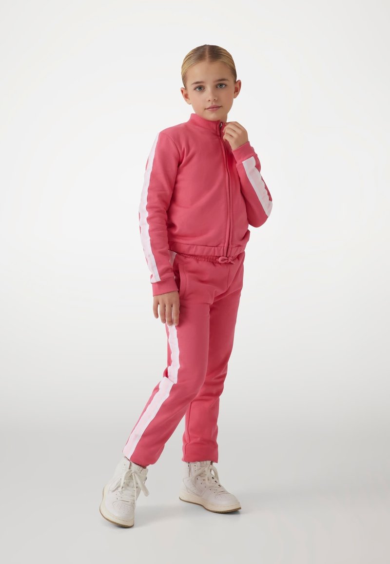 Pink tracksuit with white side stripes, made of soft material. Features a zip-up jacket and elastic waistband pants. White high-top sneakers.