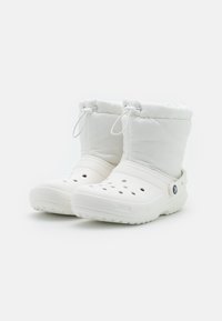 Botas de tornozelo brancas isoladas com uma base de plástico flexível, orifícios de ventilação e um cordão na parte superior para um ajuste ajustável.