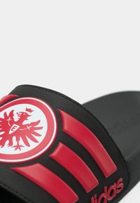 Μαύρο σανδάλι με φάσα που διαθέτει ένα ξεχωριστό κόκκινο λογότυπο αετού και τρεις κόκκινες ρίγες. Ομαλή υφή με μαλακή σόλα.