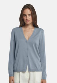 Ljusblå kofta i mjukt material med V-hals, knäppning framtill och långa ärmar. Har en rak nederkant och ribbade ärmslut.