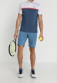 Miestenská polokošeľa s krátkym rukávom modro-bielymi pruhmi a červeným akcentom. Svetlomodré kraťasy, drží tenisovú raketu a loptičku. Biele športové topánky.