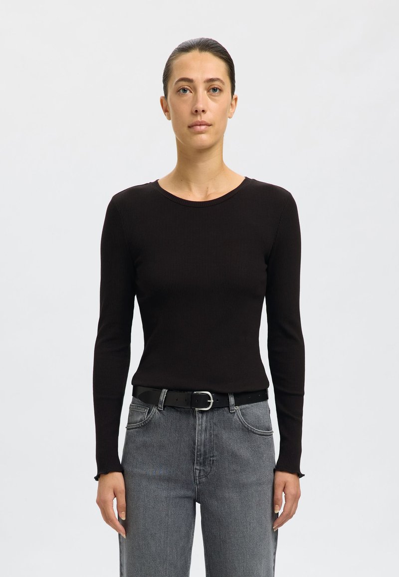 Must mustriba pikkade varrukatega särk ümmarguse kaelusega, koos hallide kõrge vöökohtadega teksade ja musta vööga hõbedase pandlaga.