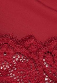 Tissu rouge avec une texture lisse et des détails en dentelle complexe sur le bord, mettant en avant des motifs floraux et des éléments ajourés.
