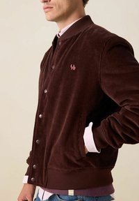 Bordeaux kleurige corduroy jas met drukknoopjes, ribbel manchetten en een klein roze logo. Beschikt over zijzakken en heeft een ontspannen pasvorm.