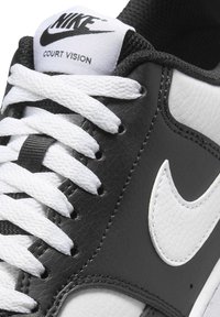 Sneaker in pelle nera con accenti bianchi, dotato di lacci bianchi piatti, logo Nike in rilievo sulla linguetta e una linea della punta elegante e arrotondata.