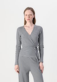 Čierno-biely pruhovaný top s dlhými rukávmi, výstrihom do V a viazaním v páse, vyrobený z jemnej a elastickej látky.