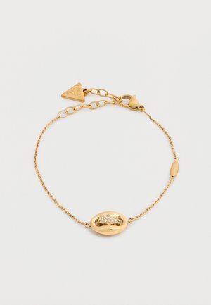 Bracelet délicat en chaîne d'or avec un centre ovale orné de petits cristaux clairs et un pendentif triangulaire de marque près du fermoir.