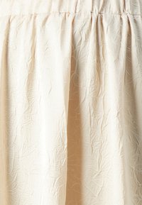 Lys beige skjørt med en rynket tekstur, med elastisk midje og en flytende design som skaper myke draperinger.