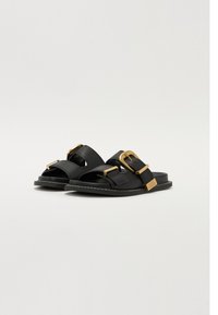 Black sandals with gold metal accents, featuring two straps and an open toe design. Smooth leather texture and contrasting white stitching detail.