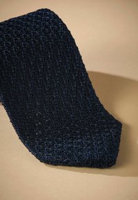 Sötétkék szőtt textil, textúrált mintával, hegyes véggel és puha, hajlékony szerkezettel, világosbarna felületen pihen.