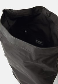 Zwarte gerecycleerde stoffen tas met een opening aan de bovenkant, een gladde textuur, een binnenzak met rits en gestikte details langs de rand.