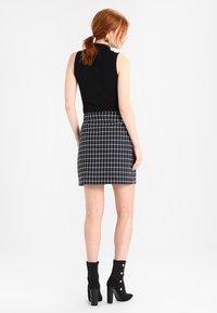 Zwart mouwloos topje gecombineerd met een zwart-wit geruite mini rok. Model draagt zwarte enkellaarsjes met knoopaccenten.