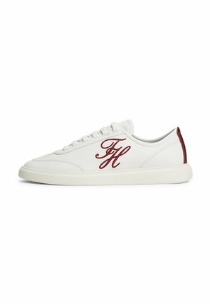 Baskets basses blanches avec initiales FH rouges brodées sur le côté et languette de talon rouge, semelle blanche et lacets blancs visibles de profil.