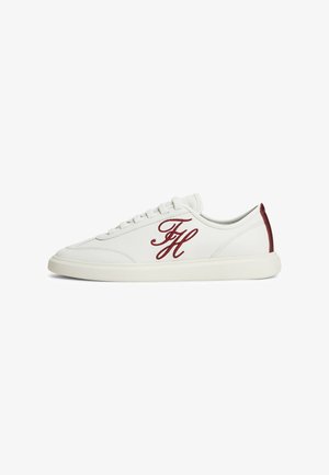 Baskets basses blanches avec initiales FH rouges brodées sur le côté et languette de talon rouge, semelle blanche et lacets blancs visibles de profil.