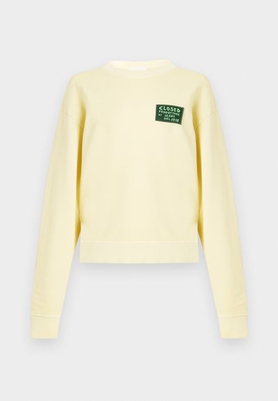 Sweat-shirt court jaune en coton, avec un col rond, des manches longues, et un patch logo vert sur le devant.