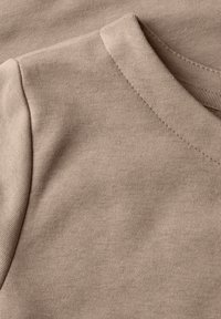 Béžová bavlněná tkanina s měkkou texturou, s klasickým kulatým výstřihem a prošívanými okraji, ukazující překrývající se design.