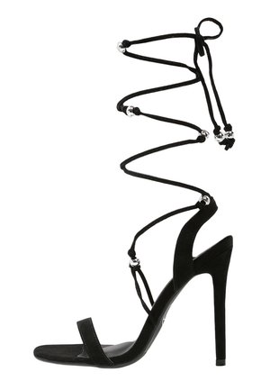 Czarny zamszowy sandał na wysokim obcasie ze smukłymi paskami wokół kostki, ozdobionymi srebrnymi koralikami, oraz eleganckim, otwartym noskiem. Charakteryzuje się obcasem typu szpilka.
