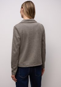 Szara teksturowana kurtka z kołnierzem, długimi rękawami i prostym dołem. Noszona z ciemnoniebieskimi jeansami.