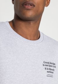 Camiseta de algodón gris con cuello redondo y mangas cortas, con un diseño de texto impreso en la parte izquierda del pecho.