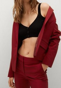 Veste rouge cintrée avec un bouton unique, assortie à un crop top noir côtelé avec des boutons sur le devant et des bretelles larges.