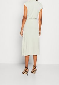 Ljusgrön knälång klänning med korta ärmar och åtsittande midja. Tyget är slätt med en flödande kjol. Färdigställd med svarta remsandaler.