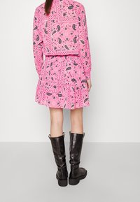 Robe rose avec des motifs paisley et en forme de cœur, jupe plissée, manches longues, associée à des bottes noires jusqu'aux genoux. Texture de tissu lisse.