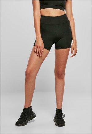 Schwarze Sportshorts aus dehnbarem Material mit hoher Taille, figurbetontem Schnitt und glatter Textur. Abgerundet mit niedrigen Sneakern.