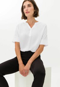Blusa blanca de manga corta, con escote en V y un corte relajado, combinada con pantalones negros ajustados. Diseño simple y minimalista.