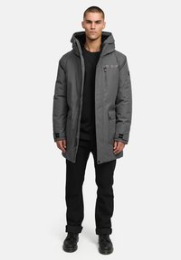 Grå isolerad parkas med huva, dragkedjestängning, sidofickor och elastiska ärmar. Buren över en svart topp och ihop med mörka byxor och stövlar.