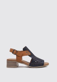 Sandale à bout ouvert en suède bleu marine et beige, dotée d'un design perforé et d'une bride ajustable à la cheville. Le petit talon empilé offre de la stabilité.
