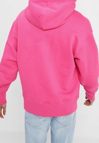 Sudadera con capucha rosa de acabado texturizado, que presenta una gran capucha, hombros caídos y puños ribeteados en el dobladillo y las mangas.