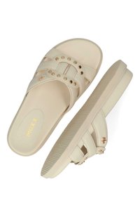 Le ciabatte beige presentano due ampie cinghie con borchie dorate, una suola piatta e texturizzata, e un branding discreto sulla soletta.