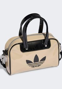 Beige patent leather bag with black accents, zip closure, dual top handles, and a prominent black logo on the front. Adjustable shoulder strap included.