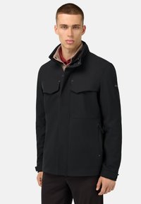 Giacca softshell nera con due tasche sul petto, colletto alto e polsini regolabili. Presenta una texture liscia e un design minimalista.