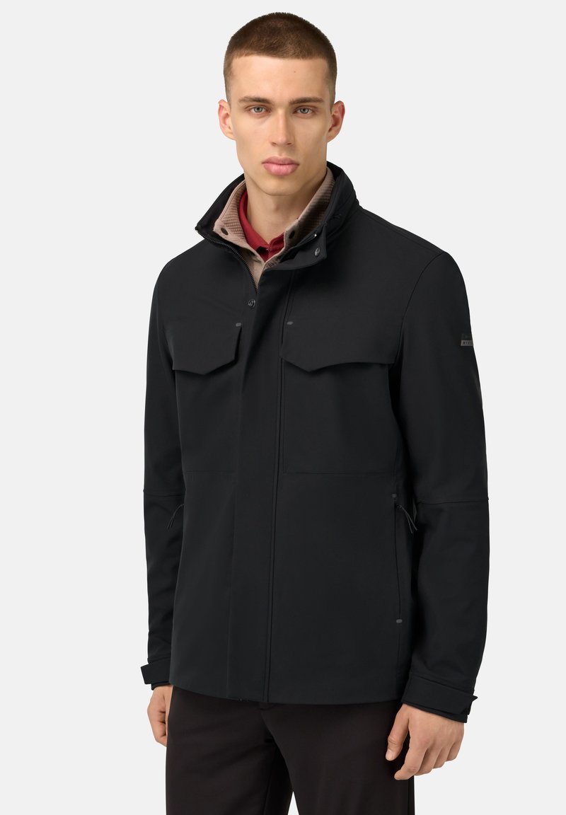 Giacca softshell nera con due tasche sul petto, colletto alto e polsini regolabili. Presenta una texture liscia e un design minimalista.