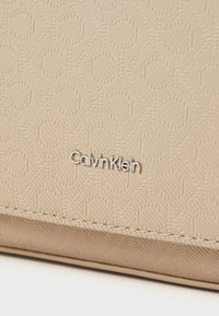 Calvin Klein beige tekstureret pung. Præget mønster med subtile linjer, sølvlogo detaljer, glat overflade og syede kanter.