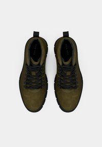 Pár olivovo zelených turistických topánok s čiernymi šnúrkami a podrážkami, pohľad zhora na bielom pozadí.