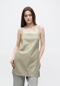 Obleka brez rokavov v barvi šalvej zelene z oglatim izrezom, gladke teksture in ohlapnega kroja, z bočnimi razporki za večjo gibljivost.