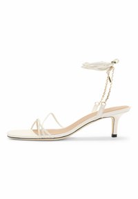 Valkoiset remmi korkokengät, joissa on ohuet remmit, neliönmuotoinen kärki, herkkä nilkkanauha tupsulla ja kultakoristeltu ketju.