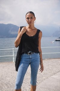 Černý texturovaný top bez rukávů s vlnitým výstřihem, spárovaný s modrými denimovými capri džínami a černým opaskem. Jednoduché šperky jako doplněk.