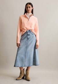 Brzoskwiniowy sweter z zamkiem błyskawicznym, jasnoniebieska spódnica w kształcie litery A oraz beżowe botki na obcasie. Miękka tekstura, luźny krój i spódnica do połowy łydki.