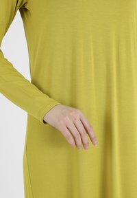 Sukienka z długim rękawem w jasnym, limonkowym kolorze, o miękkiej teksturze. Materiał gładko układa się na sylwetce, prezentując prosty i elegancki design.