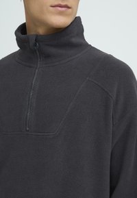 Tumehall tõmblukuga fliisisärk kõrge kraega, millel on tekstuuriga kangas ja õlal peen logo.