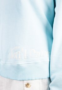 Light blue sweatshirt with ribbed cuffs and hem. Features embroidered text "I Don't Care" on the lower front in white thread.