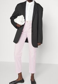 Överdimensionerad svart blazer, vit skjorta med krage, rosa raka byxor, svarta flats och en vit väskan med rynkor. Släta texturer genomgående.