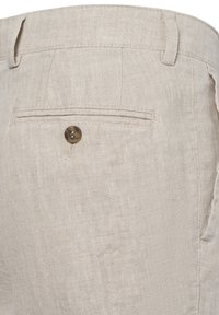 Beige Leinenhose mit strukturiertem Finish, ausgestattet mit einer einzelnen rückseitigen Tasche, die mit einem runden Bronze-Knopf gesichert ist. Maßgeschneiderter Bund.
