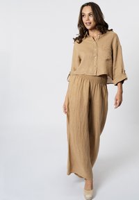 Camicia cropped in lino beige con bottoni e maniche piegate, abbinata a pantaloni in lino beige a vita alta e dalla vestibilità ampia, texture liscia.