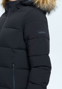 Schwarze Steppjacke mit einem gesteppten Design, ausgestattet mit einer gefütterten Kapuze, Reißverschluss-Taschen und einem Marken-Patch am Ärmel.