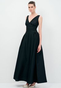 Sort gulvlængde kjole med V-udskæring, slank talje og nederdel, der går ud. Fremstillet i tekstureret stof og uden ærmer.